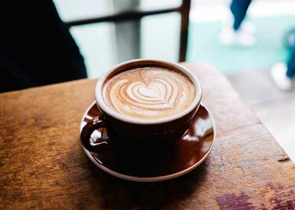 A cup of coffee with a heart design on top sits on a saucer.