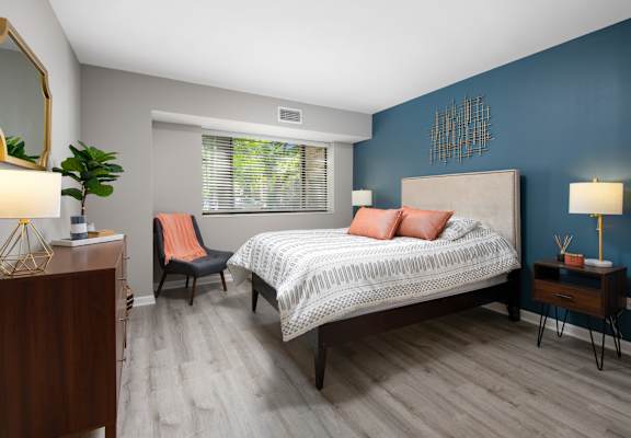 A bedroom with a bed, chair, and a plant.