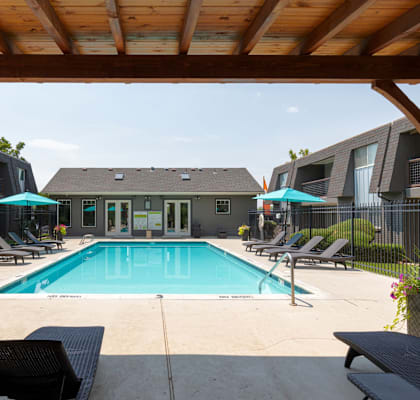 A pool area with a wooden pergola and lounge chairs.