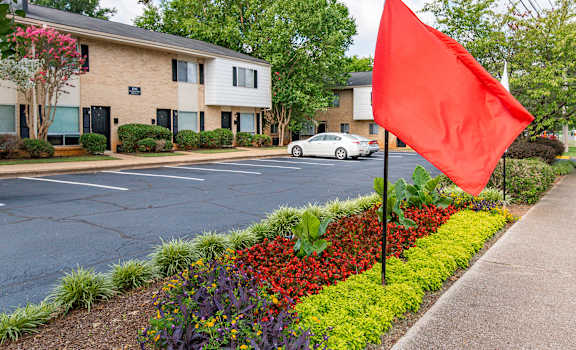 A red flag is flying in front of a building with a white car parked in front.