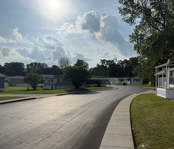 A residential street with trees and houses on both sides under a sunny sky.