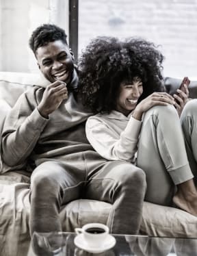 a man and woman sitting on a couch laughing and looking at a cell phone