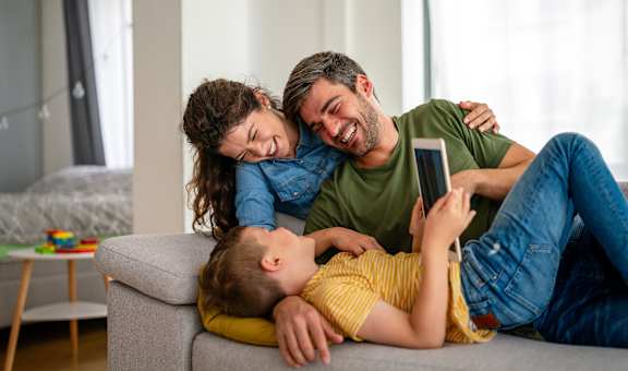 A family of three is sitting on a couch with a child in the middle.