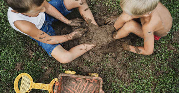 two boys playing in the dirt with shovels