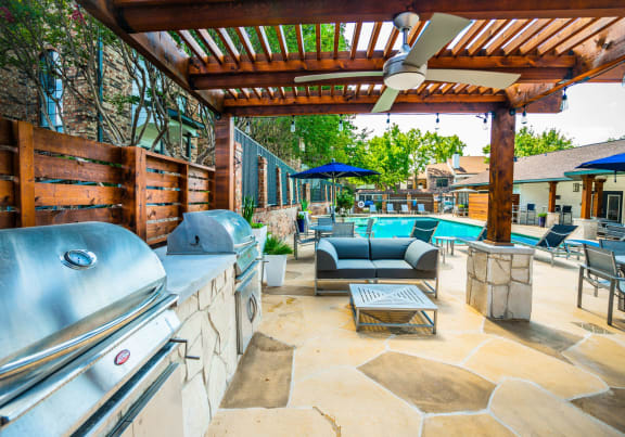 a pergola with a grill and a swimming pool in the background