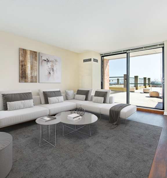 A modern living room with a white sofa, grey ottoman, and a glass coffee table.