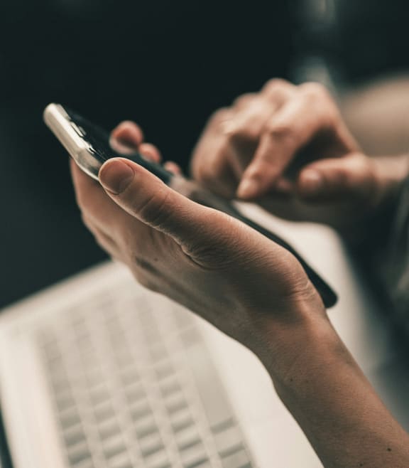 a person using a cell phone in front of a laptop computer