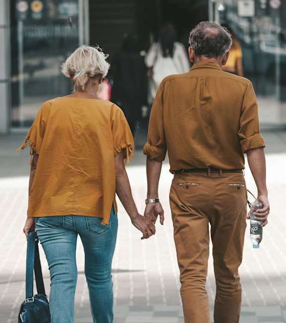 An older couple holding hands and walking down the street.