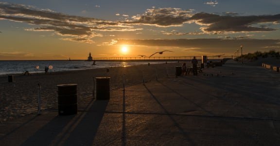 the sun sets over the beach and the ocean with a pier in the background at Normandy Village Apartments, Michigan City, IN
