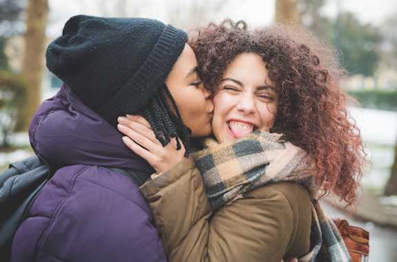 A person in a purple jacket is hugging another person in a brown jacket and a plaid scarf.