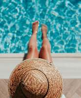 A person wearing a straw hat is sitting by a pool.