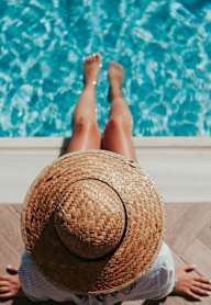 A person wearing a straw hat is sitting by a pool.