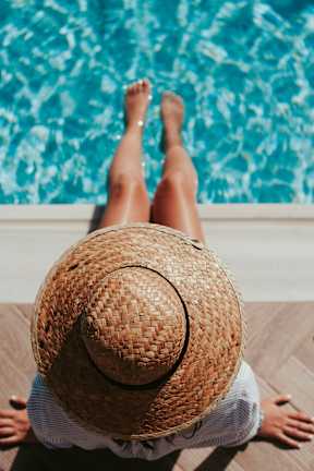 A person wearing a straw hat is sitting by a pool.