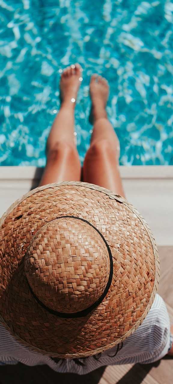 A person wearing a straw hat is sitting by a pool.