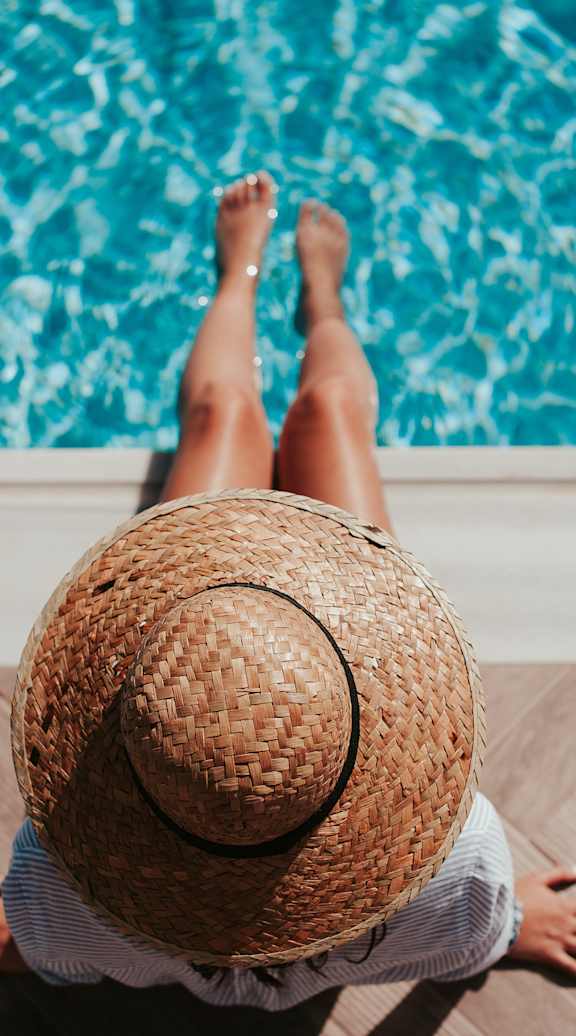 A person in a sun hat sitting on the sundeck at a resort style pool at a luxury apartment community