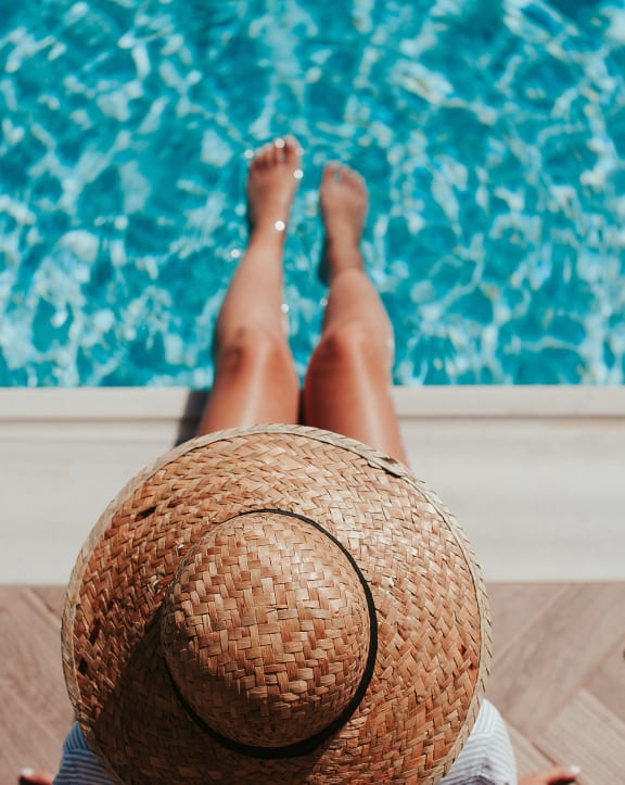 a woman with a straw hat laying by a pool