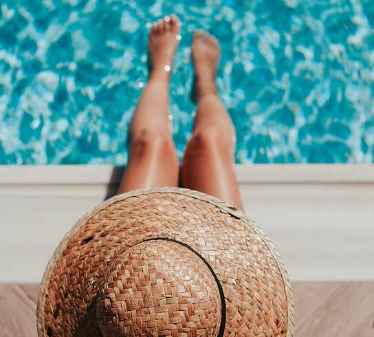A person wearing a straw hat is sitting by a pool.