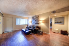 Large Living Room with Hardwood Inspired Floors, Open Windows, Black Sofa with 1 Lamps on Each Side, View of Hallway Leading to Bedroom