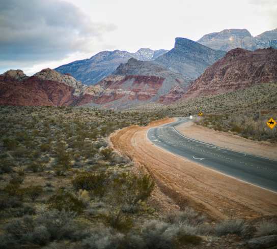 A winding road in a desert with mountains in the background.