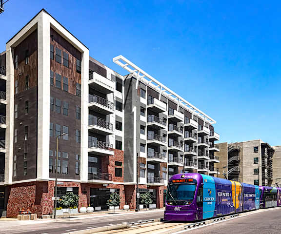 A purple train is on the tracks in front of a building.