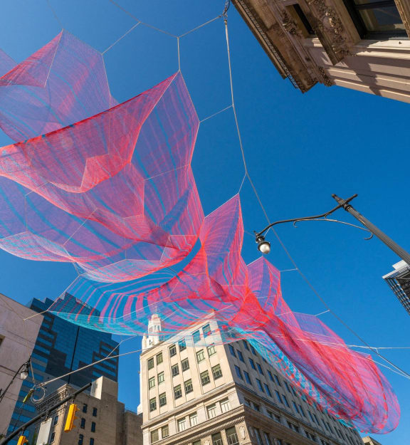a large red and blue kite flying over a city street at The Madison, Columbus, OH, 43215