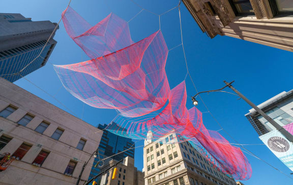 a large red and blue kite flying over a city street at The Madison, Columbus