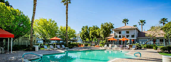 A pool surrounded by palm trees and a red umbrella.