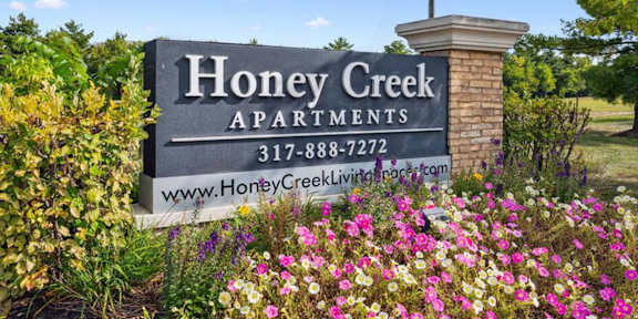 A sign for Honey Creek Apartments is surrounded by flowers.