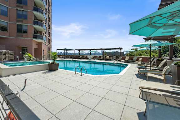A pool surrounded by a patio with chairs and umbrellas.