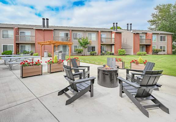 A patio with chairs and a fire pit in front of apartment buildings at Pointe East Apartments in Fife, WA.
