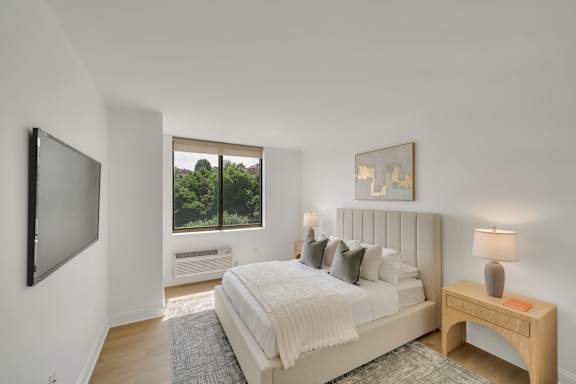 A bedroom with a large bed, a flat screen TV, and a window with a view of trees.