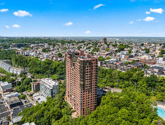 A tall red brick building stands out in a cityscape surrounded by green trees.