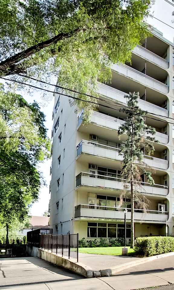 A tall residential building with balconies and a black fence in front.
