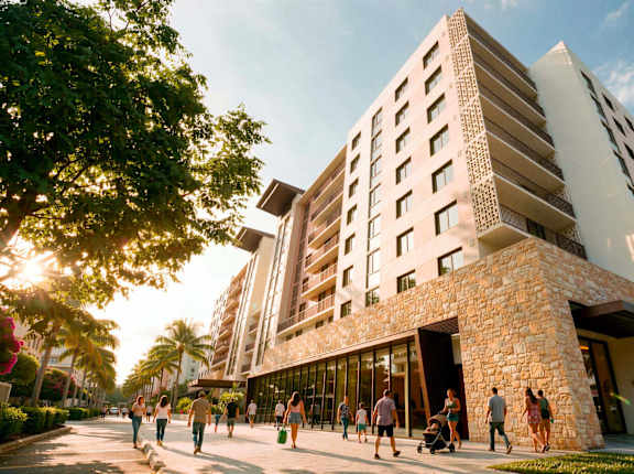 A modern building with a stone facade and large windows is surrounded by people walking on the sidewalk.