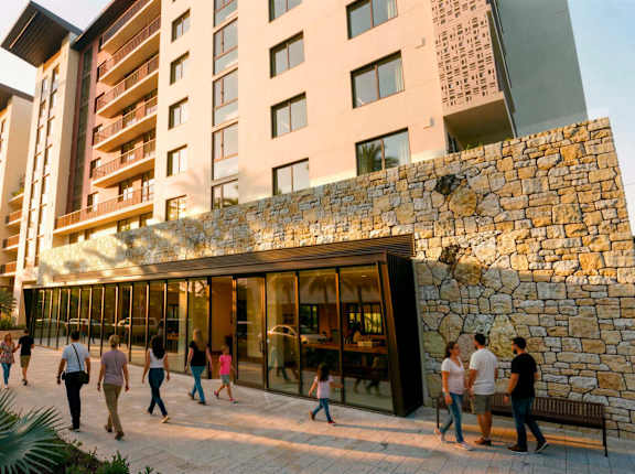 A group of people are walking in front of a building with a stone wall.