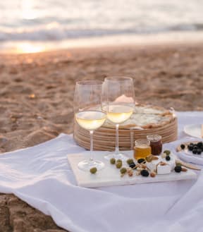 a romantic dinner on the beach with two glasses of wine and a cheese board