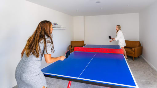 two women playing a game of ping pong on a blue table