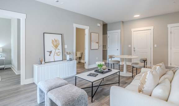 A living room with a white couch, a coffee table, and a grey ottoman.