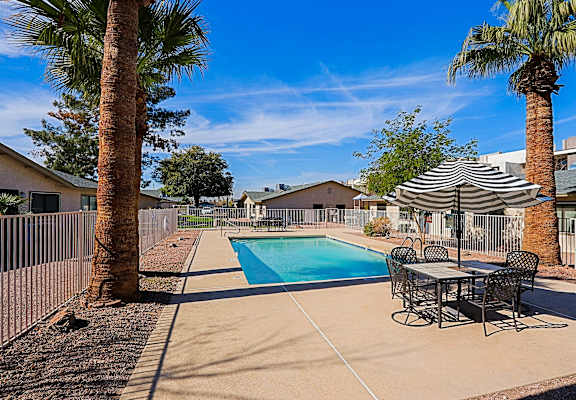 A pool surrounded by a table and chairs and palm trees.