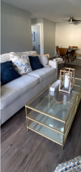 A white couch with blue pillows sits in a living room with a glass coffee table.
