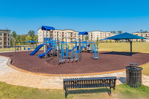 a playground with blue playset and umbrellas in front of apartments