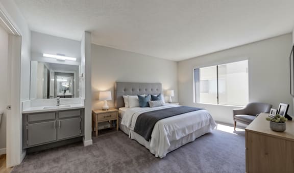 A bedroom with a large bed, a chair, and a vanity with a mirror.
