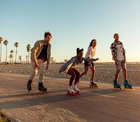 Four people roller skating on a beach at sunset.