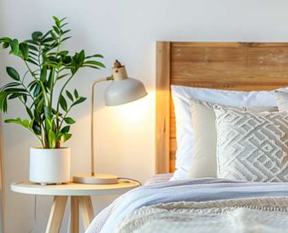 a bedroom with a bed and a table with a lamp and a plant