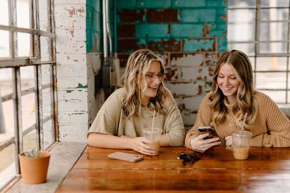 Two women sitting at a table with drinks and a smartphone.