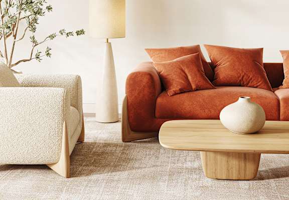 A living room with a white couch, a brown couch, a white lamp, and a white vase on a wooden coffee table.