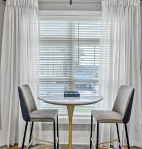 a table with two chairs in front of a window with white curtains