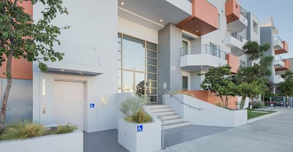 A modern building with a white and orange exterior and a tree in front at Woodley Sara Apartment, Van Nuys, 91406