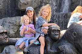 A woman and two children are sitting on a gorilla statue.