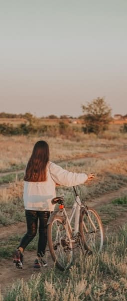 a woman walking a bike down a dirt road